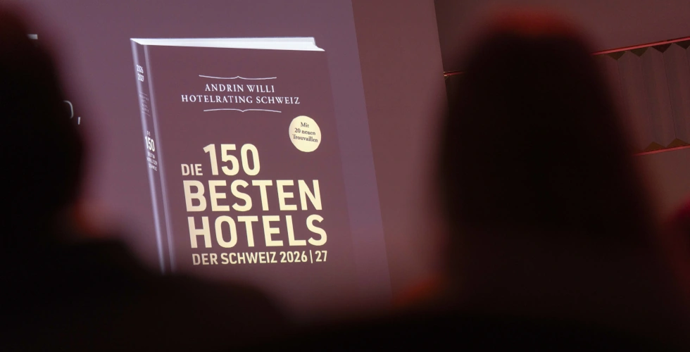 Hoteliers des Jahres - eine unfassbare Ehre für uns, das gesamte Team und Sie, unsere Gäste! 2 Foto aus den Zuschauerrängen in Richtung Bühne, im Vordergrund 2 schwarze Köpfe, im Hintergrund ein Buch-Cover